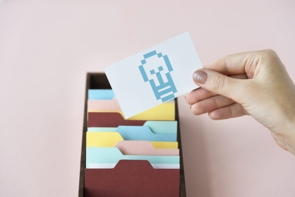 ファイルボックスから電球のアイコンが描かれたカードを取り出す手元。マージコンビニ攻略のコツや効率的な進め方のヒントを整理しているイメージ。