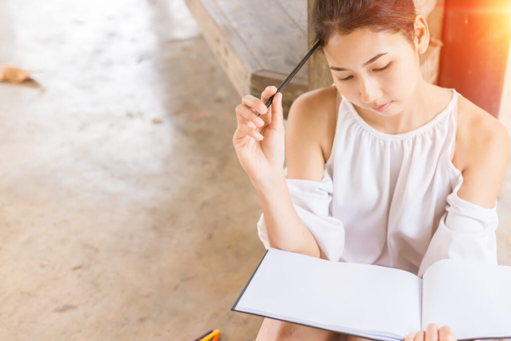 ノートを広げてペンを片手に考え込む女性。マージコンビニのポイ活で、レベル36の壁や難しい注文をどう乗り越えるか攻略法を練っている様子。