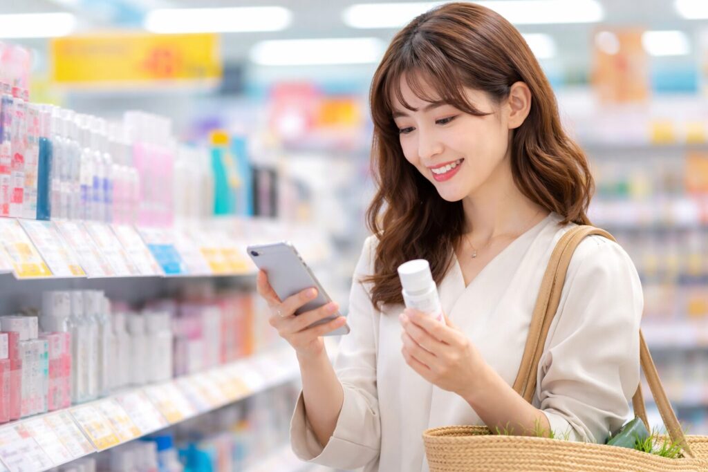 マツキヨの店内でスマホを見ながら化粧品を選ぶ日本人女性