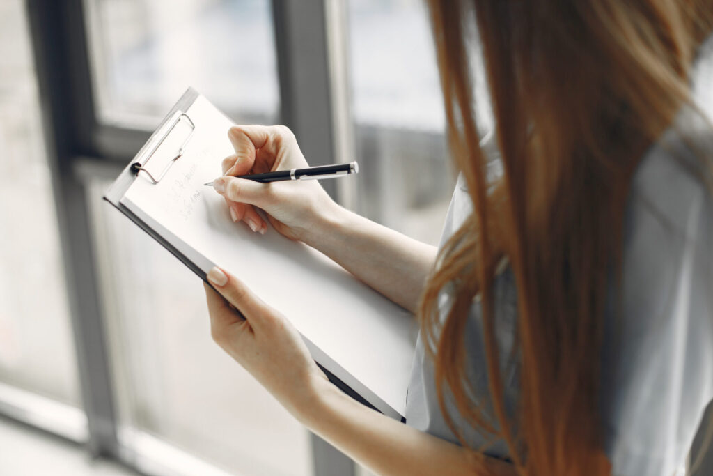 クリップボードに何かを書き込んでいる女性の手元のクローズアップ。